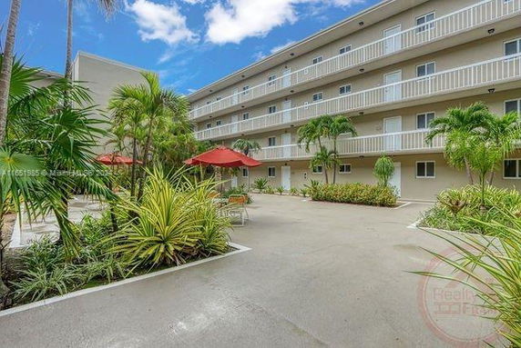 View of a multi-story building with balconies and a courtyard area with plants and outdoor seating.