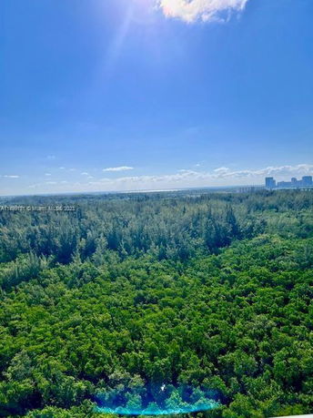 Panoramic view of a forested area with distant buildings and a clear blue sky.