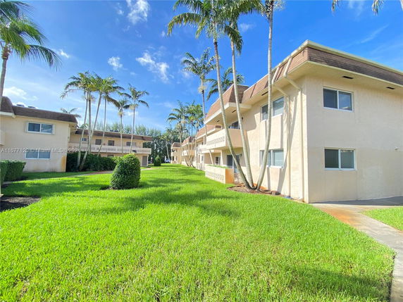 Front view of a multi-story residential building with a sloped roof and surrounding greenery.