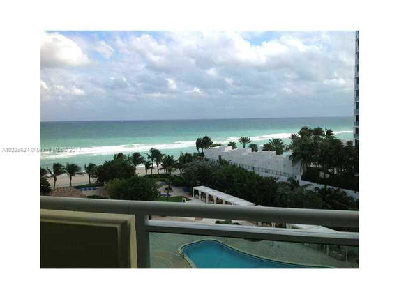 Panoramic view of the ocean and beach with nearby buildings and pool area.