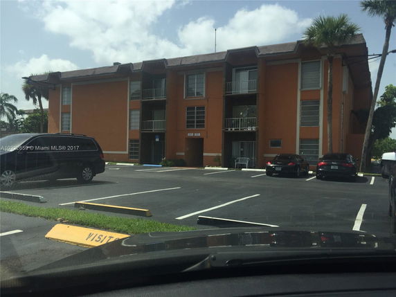 Front view of a three-story apartment building with balconies and parking spaces.