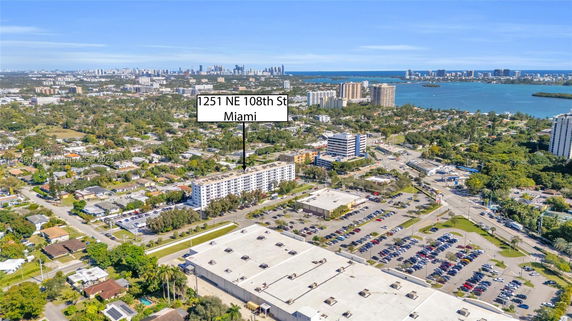 Aerial view of a residential and commercial area with a large building in the center and a body of water in the background.