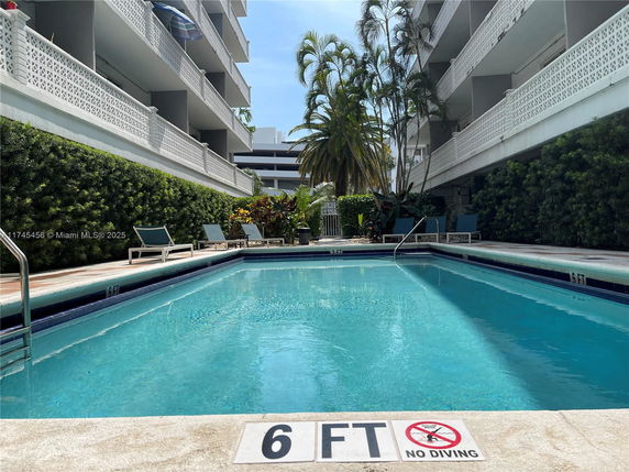 Outdoor swimming pool area with lounge chairs surrounded by apartment buildings.