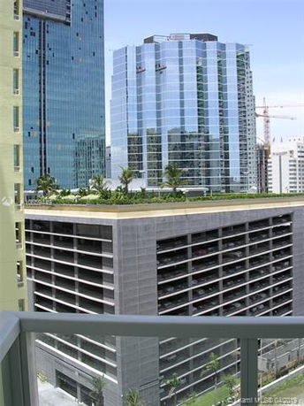 View of a modern urban area featuring a multi-story parking structure with a rooftop garden and adjacent high-rise office buildings with reflective glass exteriors.