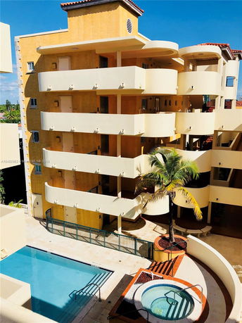 Front view of a multi-story building with yellow walls and white balconies, featuring an outdoor swimming pool and a hot tub.