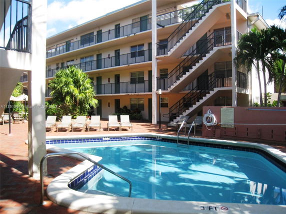 Outdoor swimming pool surrounded by a multi-story apartment building with balconies.
