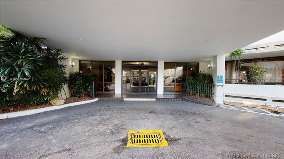 Front entrance of a building with glass doors and surrounding greenery.