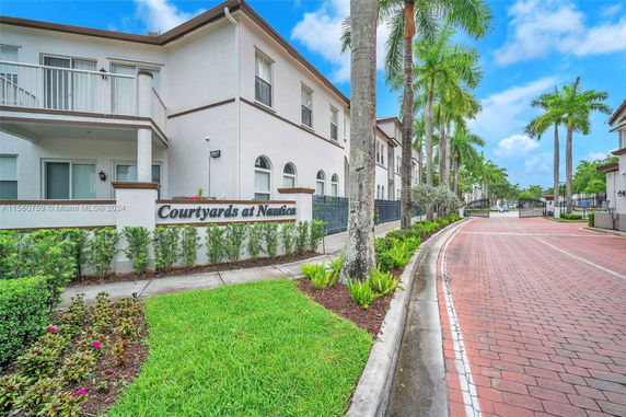 Front view of a two-story residential building with a pathway and palm trees.