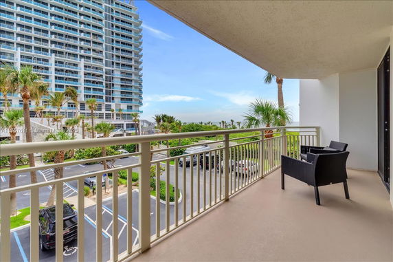 Balcony view of a high-rise building with a parking area and palm trees.