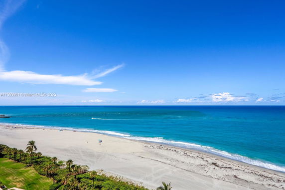Wide view of a sandy beach and ocean under a clear blue sky.