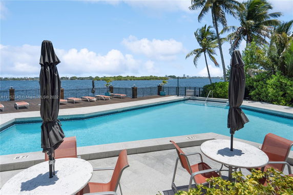 Outdoor swimming pool area with lounge chairs and umbrellas, overlooking a waterfront view.
