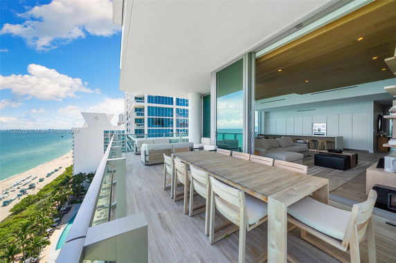 Panoramic view of ocean from a modern balcony with outdoor seating and dining area.