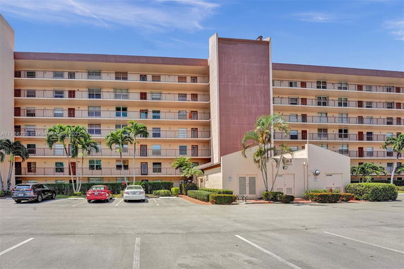 Front view of a multi-story apartment building with balconies and a parking area.