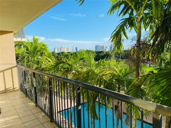 View from a balcony overlooking trees and distant buildings under a blue sky.
