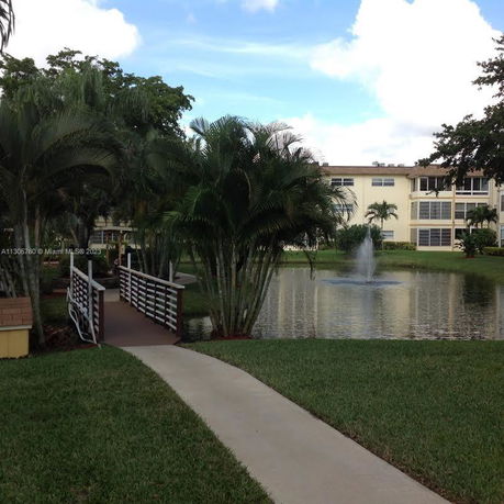 View of a pond with a fountain and a bridge leading to a building.