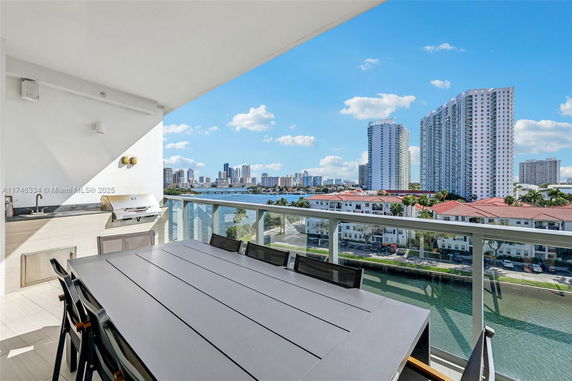 View from a balcony with dining table, grill, and cityscape across a waterway.