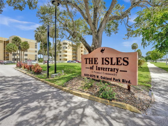 Front view of a multi-story residential building with a community sign in the foreground.