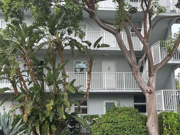 Front view of a multi-story building with white railings and trees in front.