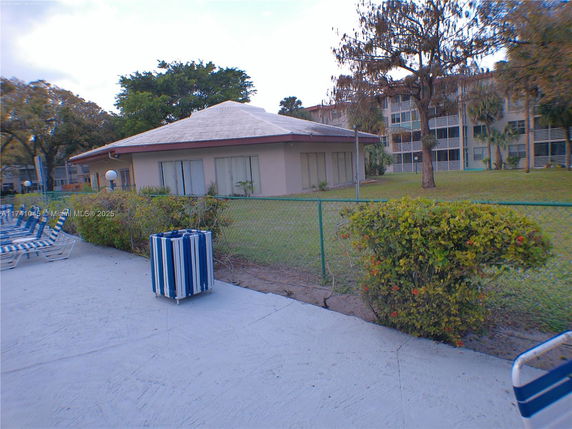 View of a building with a sloped roof and patio area surrounded by a fence.