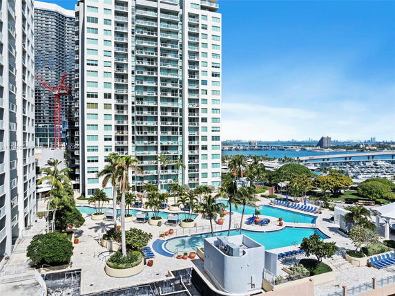View of tall residential buildings, swimming pool area, and waterfront with marina in the background.