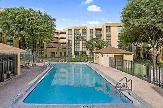 Outdoor swimming pool area adjacent to a multi-story building with large glass windows.
