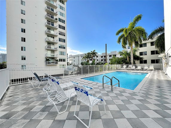 Outdoor swimming pool area with lounge chairs next to a multi-story building.