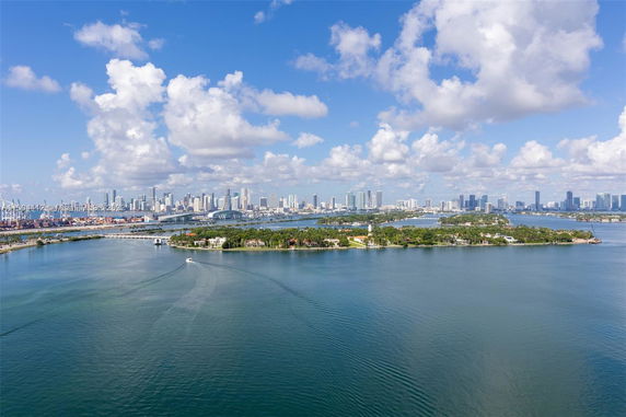 Panoramic view of water with islands and distant city skyline under a partly cloudy sky.