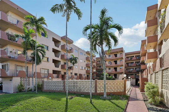 Front view of a multi-story residential building with balconies and palm trees.