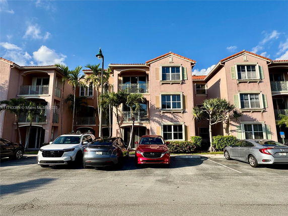 Front view of a three-story residential building with balconies and parking area.