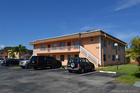 Front view of a two-story building with external stairs and parking area.
