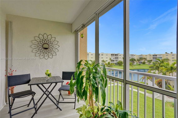 View from a balcony with outdoor furniture overlooking a grassy area and buildings.