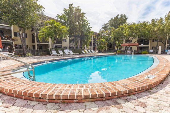 Outdoor swimming pool area with lounge chairs and apartment buildings in the background.