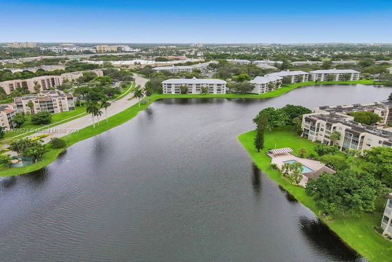 Aerial view of residential buildings surrounding a lake, with roads and trees visible.