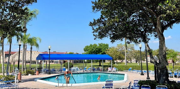 Outdoor swimming pool area with a blue canopy, surrounded by trees and lounge chairs.