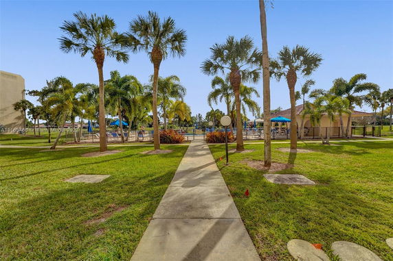 View of a swimming pool surrounded by palm trees and grassy area with a pathway leading to it.