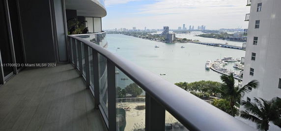 Partial view from a building balcony overlooking a body of water and cityscape in the distance.