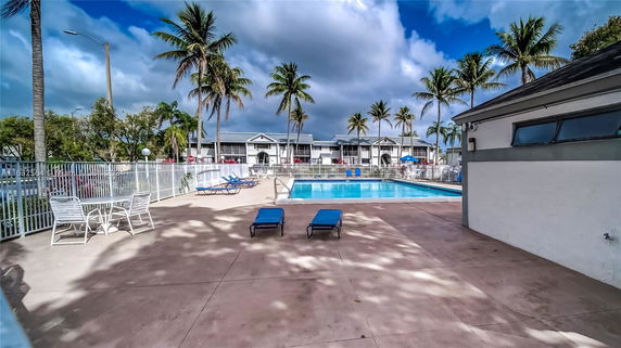 Outdoor swimming pool area with lounge chairs and palm trees.