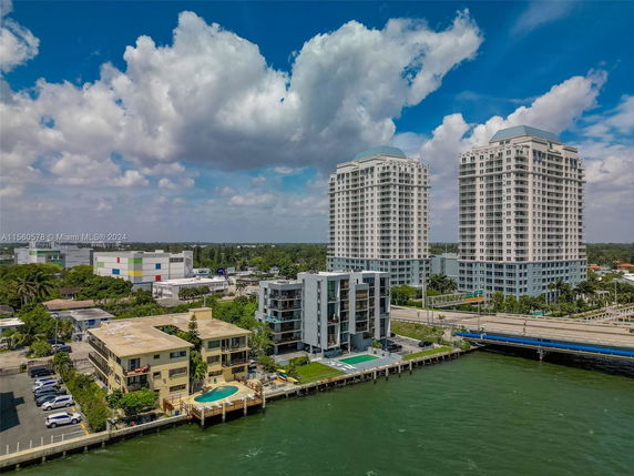 Aerial view of waterfront buildings with swimming pools and high-rise structures in the background.