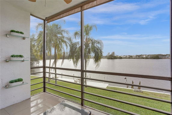 View from a screened-in balcony overlooking a body of water with palm trees in the foreground.