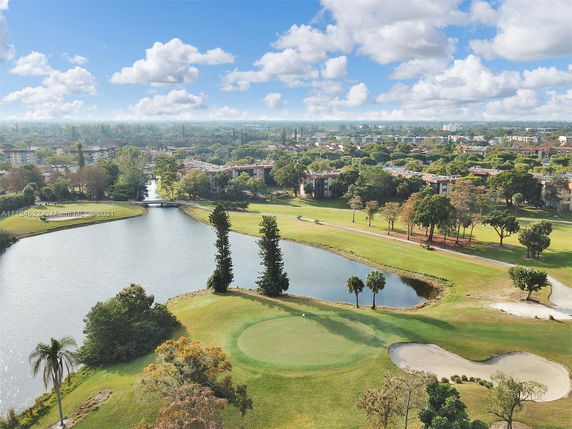 Panoramic view of a golf course with a water body and surrounding residential buildings.