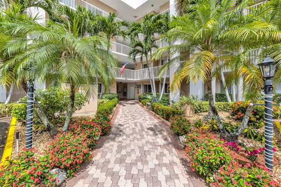 Front view of a multi-story building with balconies and tropical landscaping.
