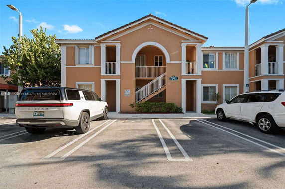 Front view of a two-story building with arched balconies and parking spaces.