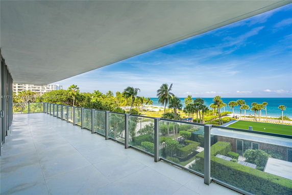 Wide angle view of the ocean and surrounding greenery from a building balcony.