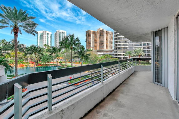 Balcony view overlooking a landscaped area with tall buildings and palm trees in the background.