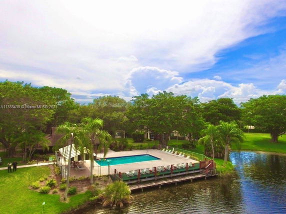 Outdoor swimming pool area beside a body of water with surrounding greenery.