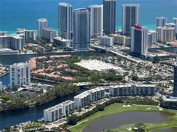 Aerial view of a cluster of high-rise buildings with a golf course and water body in the foreground.