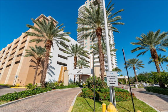 Front view of a modern high-rise building with palm trees and a driveway.