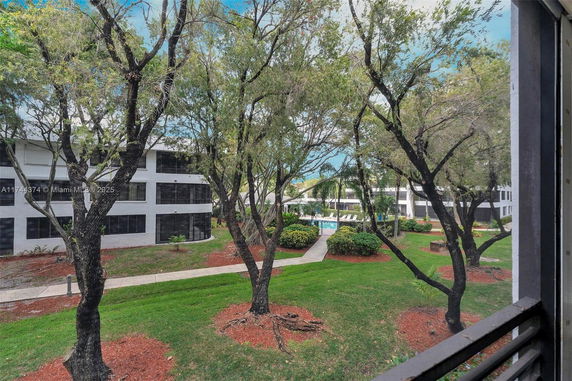 View from a building showing an outdoor area with a swimming pool surrounded by trees and landscaped greenery.