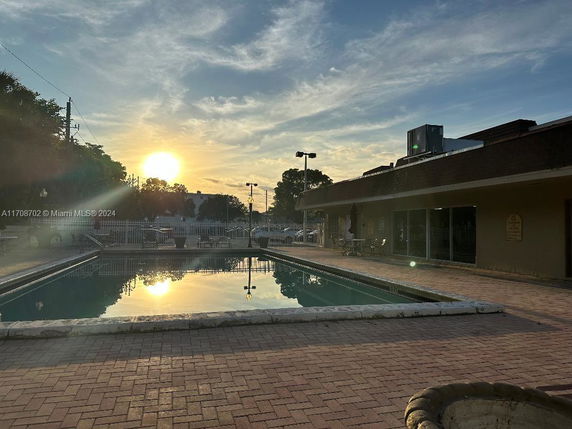 Outdoor swimming pool area with brick paving and a building adjacent.