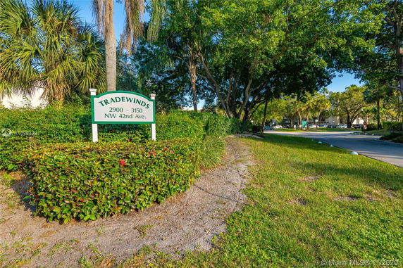 Signage for Tradewinds with surrounding greenery and a roadway.
